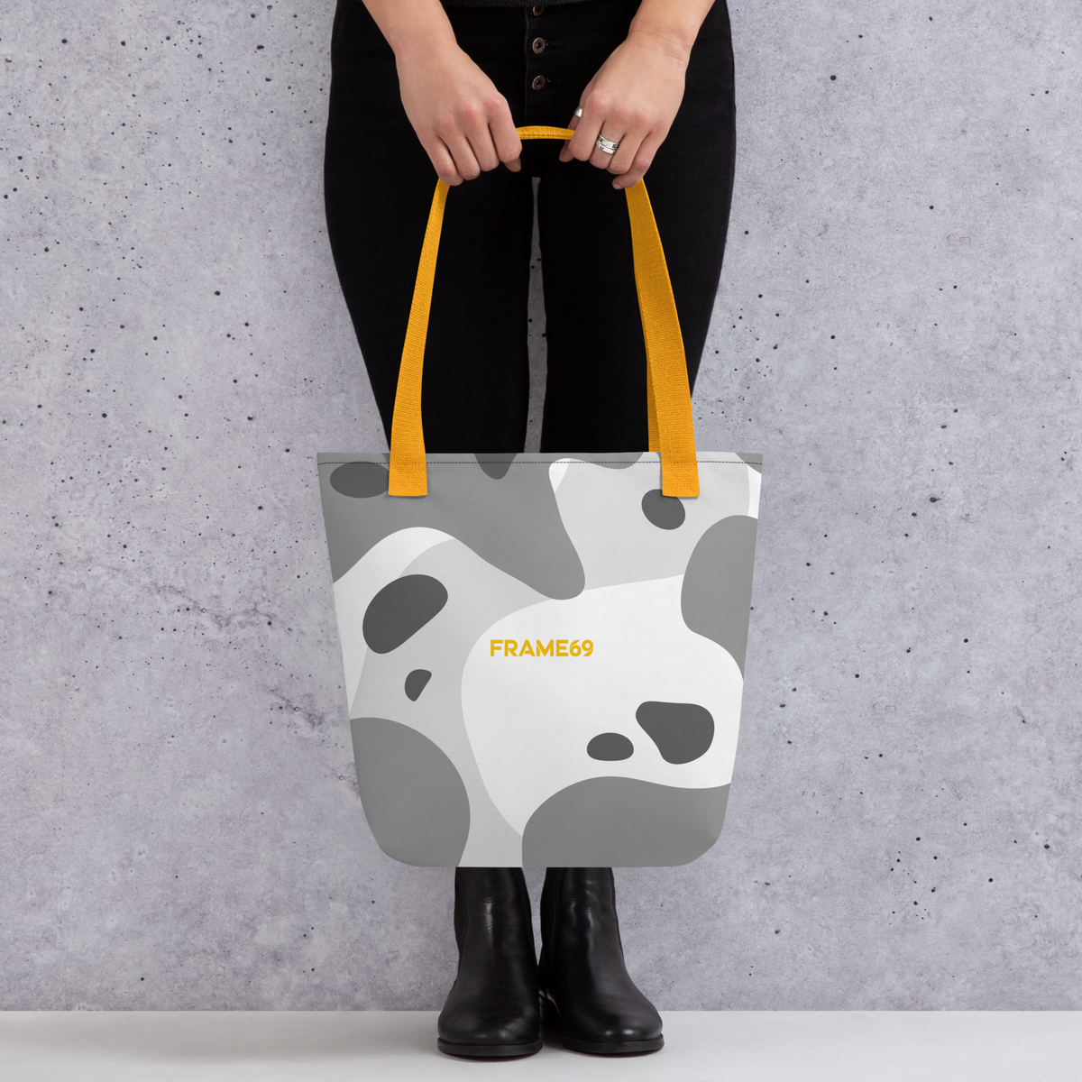 White graphic tote bag with yellow handles, abstract cow print, FRAME69 logo.